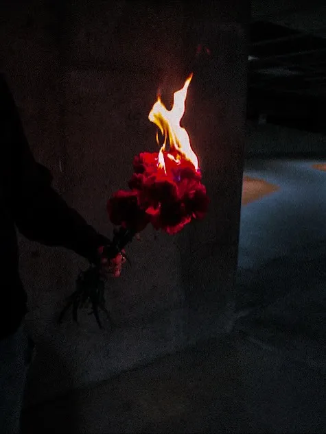 A hand holding a burning bouquet of red carnations in a dark parking garage